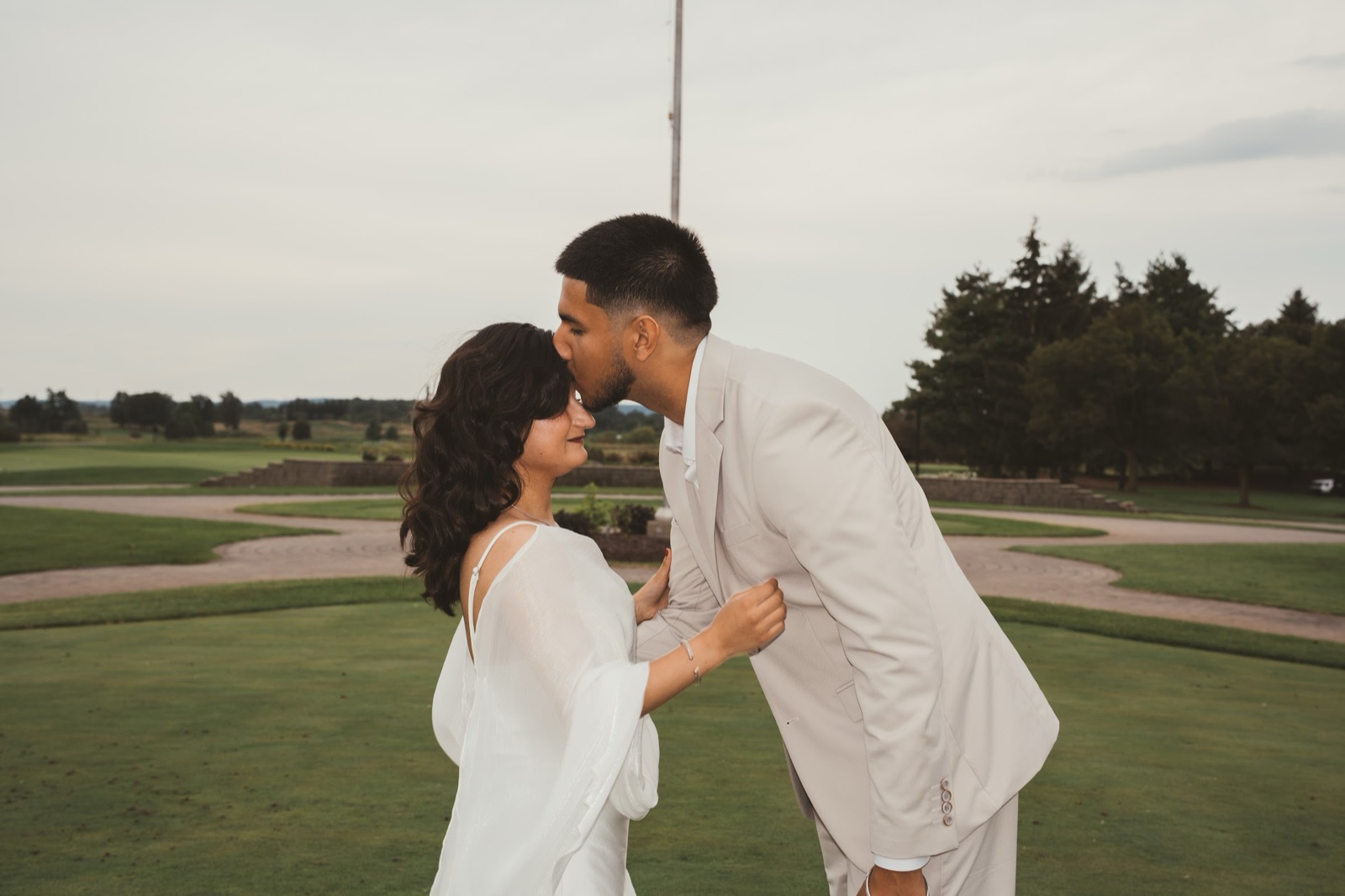 Groom kissing the bride's forehead on a golf course